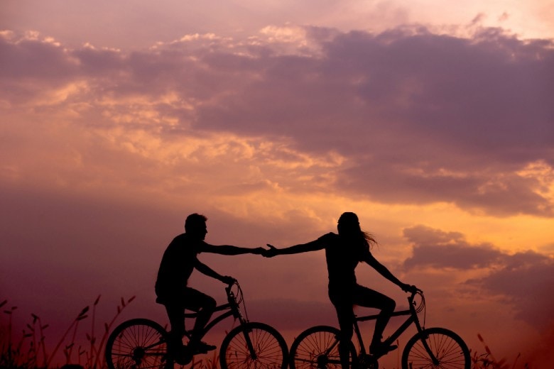 Couple cycling at sunset while holding hands